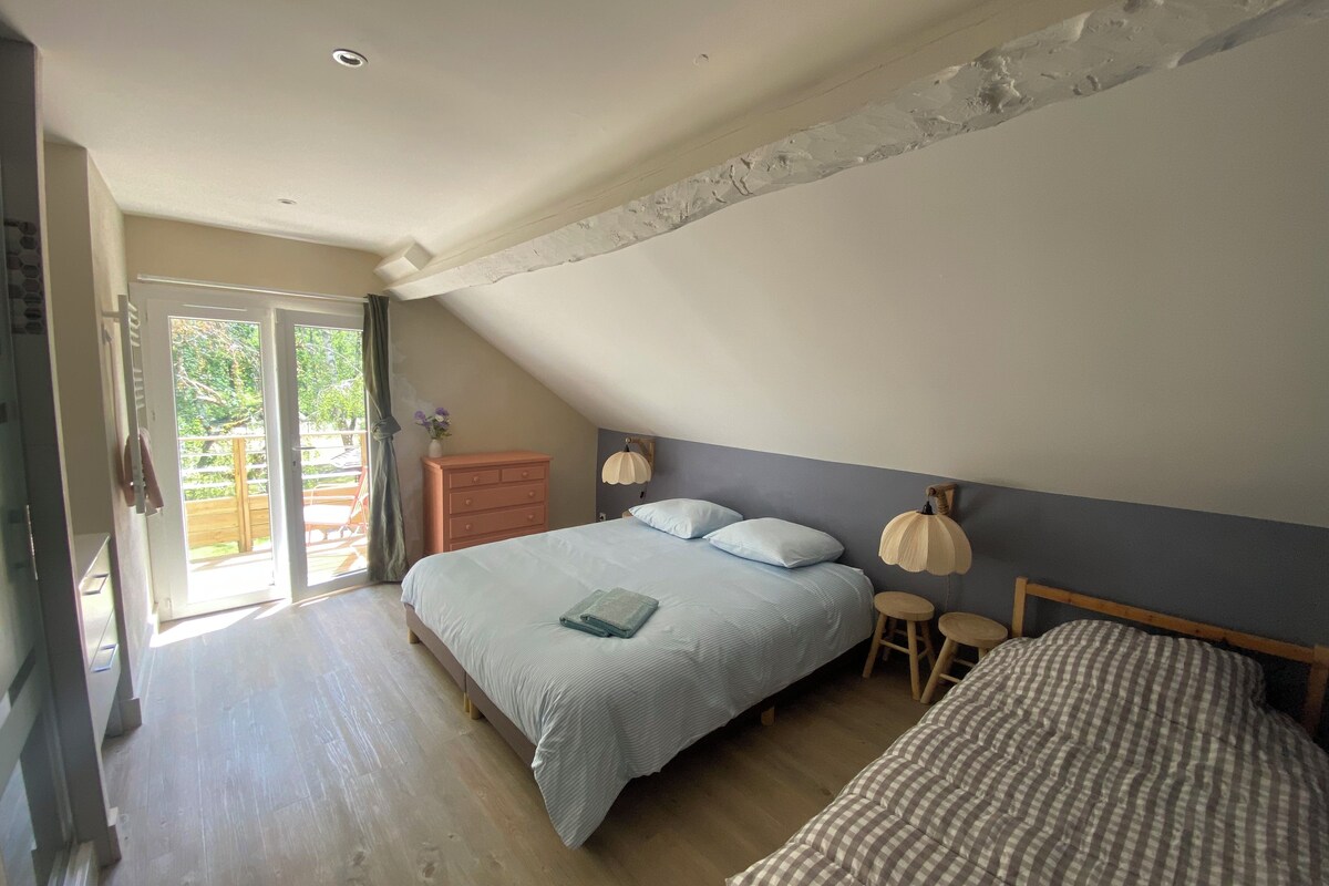 Un dormitorio con techo inclinado, una cama con colcha azul, un aparador y una mesita de noche con lámpara.