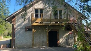 Un edificio de piedra rústica con un balcón de madera, una entrada central y un área pavimentada al frente.