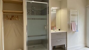 Un baño con ducha de vidrio, tocador con espejo y perchero para toallas.