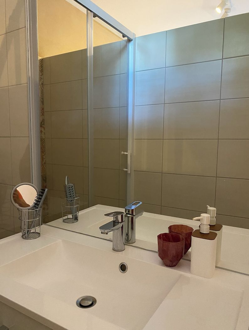 Une salle de bain avec un lavabo blanc, un miroir, un porte-serviettes et un espace douche.