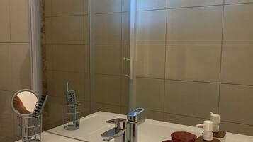 Une salle de bain avec un lavabo blanc, un miroir, un porte-serviettes et un espace douche.