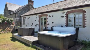 En bygning i sten med træterrasse, jacuzzi og en stenvæg med blomster.