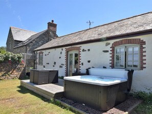 A stone building with a wooden deck, a hot tub, and a stone wall with flowers. - 2 Bed in St. Agnes (oc-50085) (Saint Agnes)