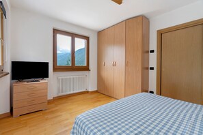 A bedroom with a bed, a dresser, a television, a window with a mountain view, and a wardrobe.