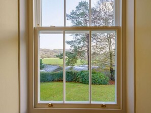 Ein Fenster mit Blick auf eine grüne Landschaft, darunter Bäume und eine Wiese.