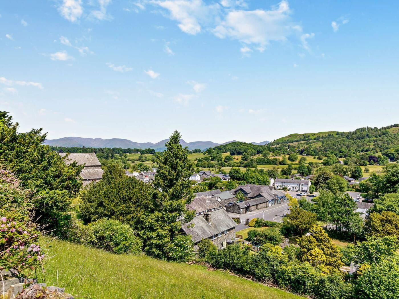 A rural village with stone houses, green fields, and hills in the background.