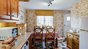 A kitchen with wooden cabinets, a dining table with chairs, a microwave, a bread loaf, and a patterned wallpaper. - 2 Bed in Hawkshead (oc-llh29) (Hawkshead)