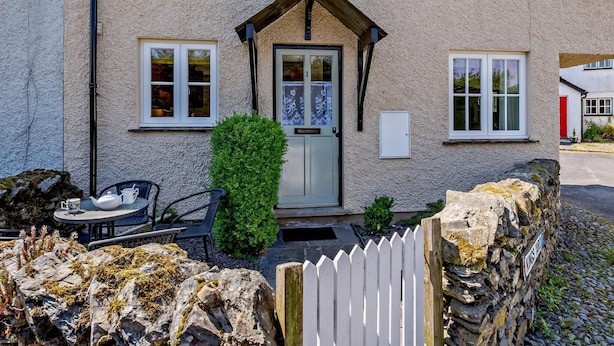 A house with a stone wall, a white picket fence, a door with a glass panel, and a small garden with a table and chairs. - 2 Bed in Hawkshead (oc-llh29) (Hawkshead)