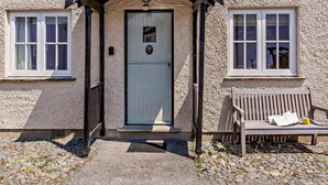 A building with a textured facade, a white door, and a small porch with a bench. - 2 Bed in Hawkshead (oc-llh29) (Hawkshead)