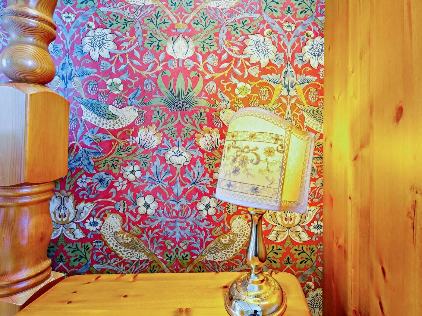 Una mesa de madera con una lámpara decorativa y un fondo de papel tapiz estampado.