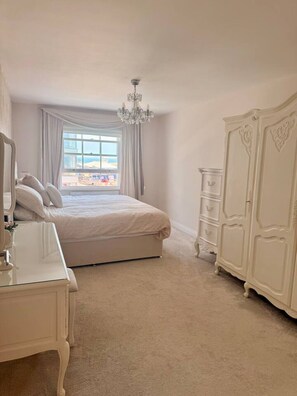 Une chambre à coucher avec un lit, une commode, un miroir, un lustre et une vue sur l’extérieur.