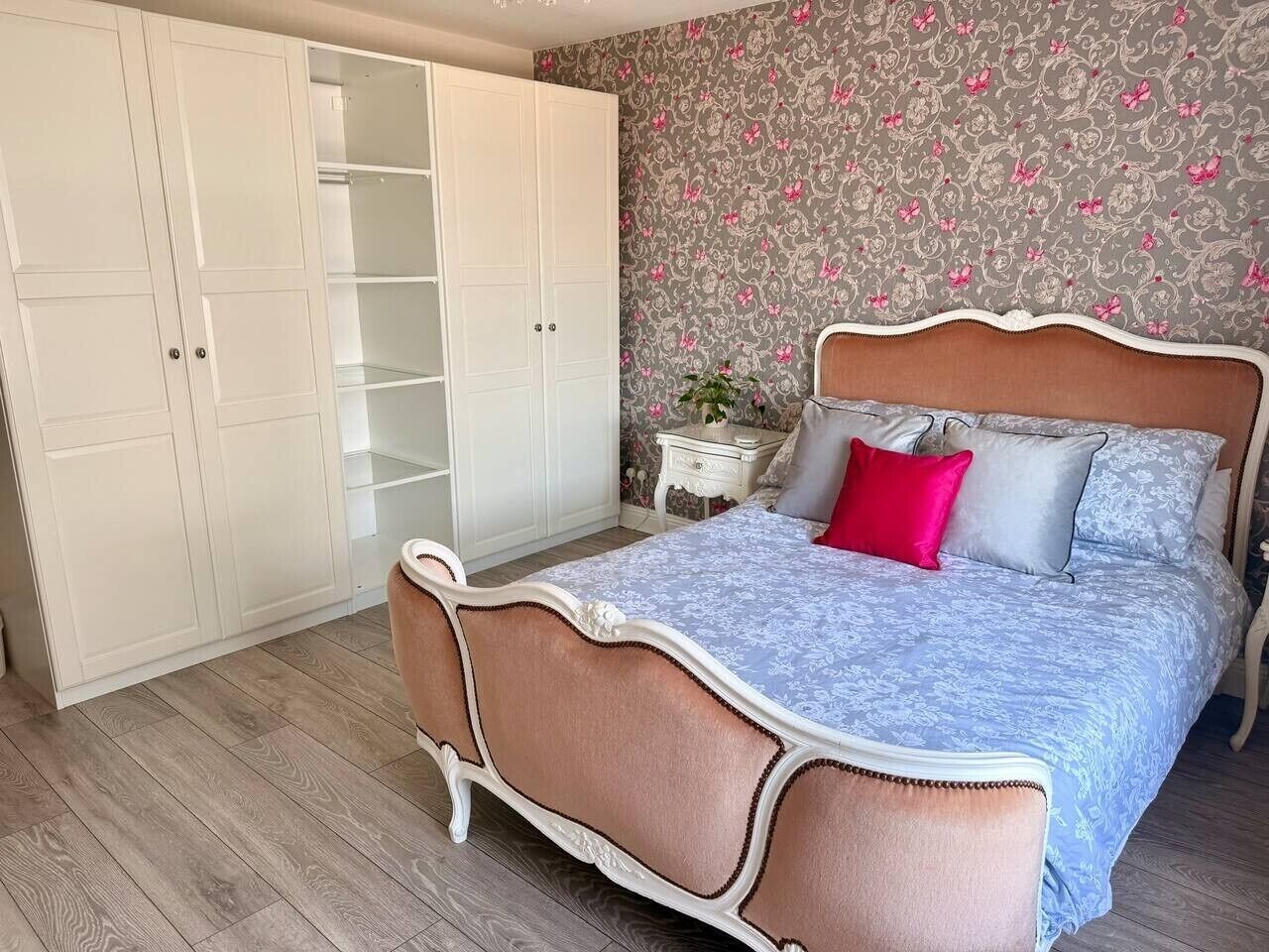 Een slaapkamer met een bed, een kledingkast, een nachtkastje en bloemenbehang.