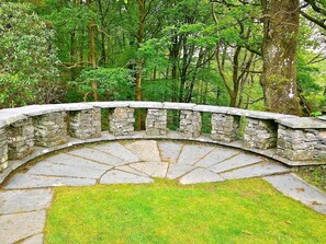 Eine steinerne Brücke mit geschwungener Form, umgeben von üppigem Grün und Bäumen.