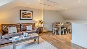 A modern living room with a leather sofa, a dining table, and a kitchen area. - 2 Bed in Saundersfoot (oc-50550) (Saundersfoot)