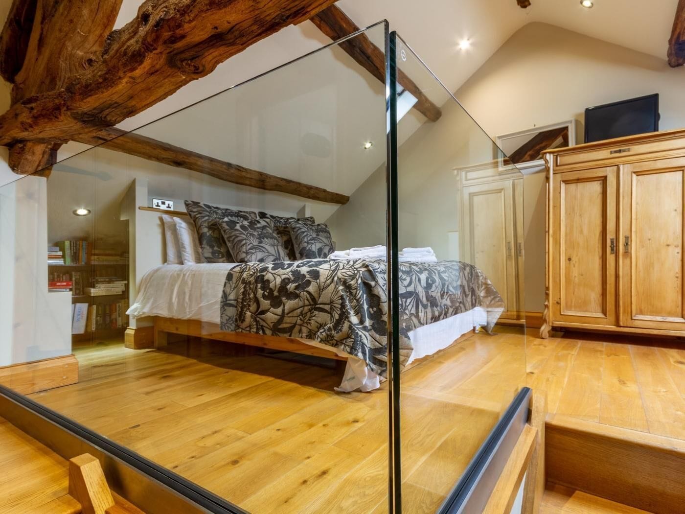 Ein Schlafzimmer mit einem Bett, Holzboden, einer Glastrennwand und einem Holzbalken an der Decke.