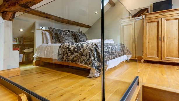 Une chambre avec un lit, un plancher en bois, une cloison en verre et une poutre en bois au plafond.