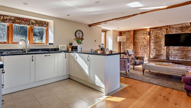Una cocina moderna con armarios blancos, una isla central y una zona de comedor con sofá y televisor de pantalla plana.