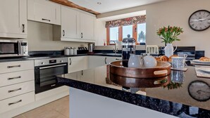 Una cocina moderna con armarios blancos, encimera negra, cafetera, hervidor y un reloj en la pared.
