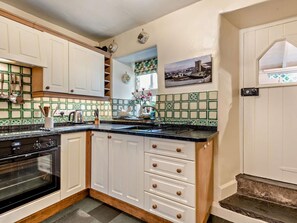 A kitchen with white cabinets, a black stove, and a tiled backsplash. - 3 Bed in Hawkshead (oc-llh34) (Hawkshead)
