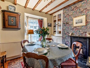 Ein Esszimmer mit Esstisch für vier Personen, Kamin, Bücherregal und Fenster mit Vorhängen.