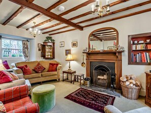 A cozy living room with a fireplace, wooden beams, a sofa, a green ottoman, and a bookshelf. - 3 Bed in Hawkshead (oc-llh34) (Hawkshead)