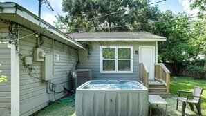 Un jacuzzi en un patio trasero con una terraza de madera y una casa pequeña.
