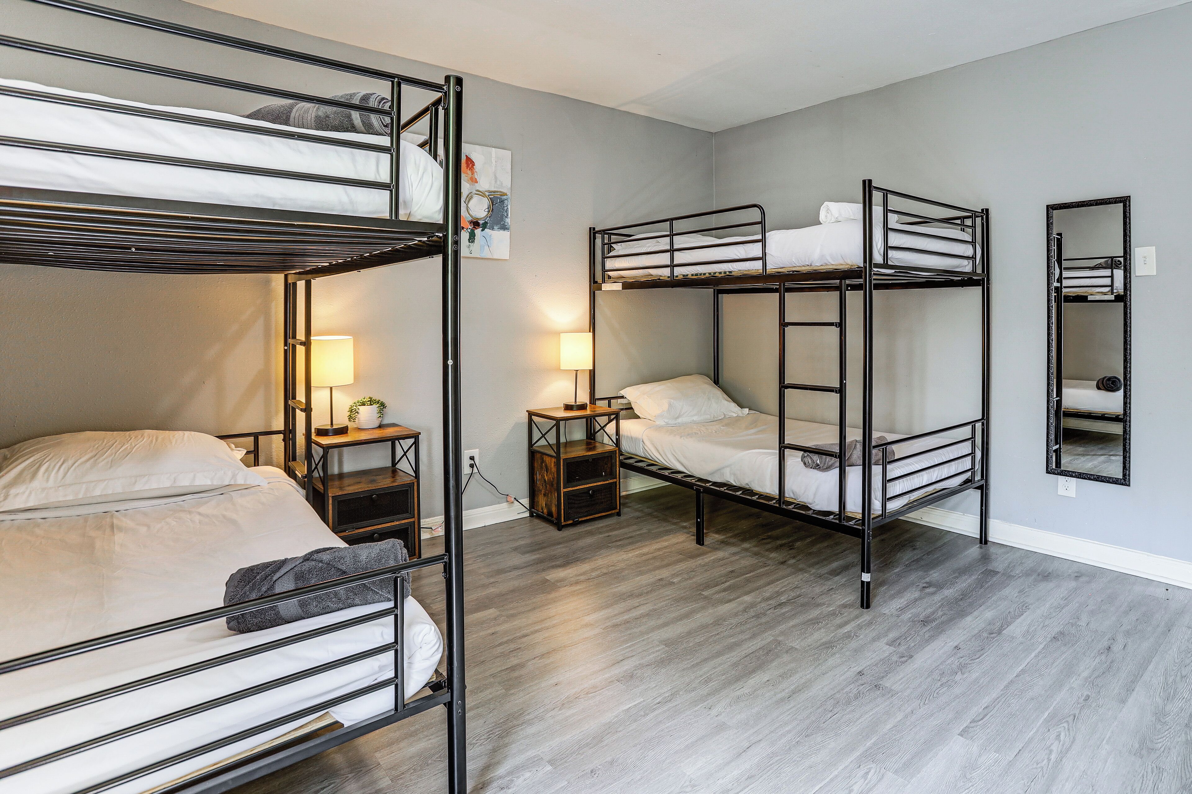 A room with bunk beds, a bedside table with a lamp, and a mirror on the wall.