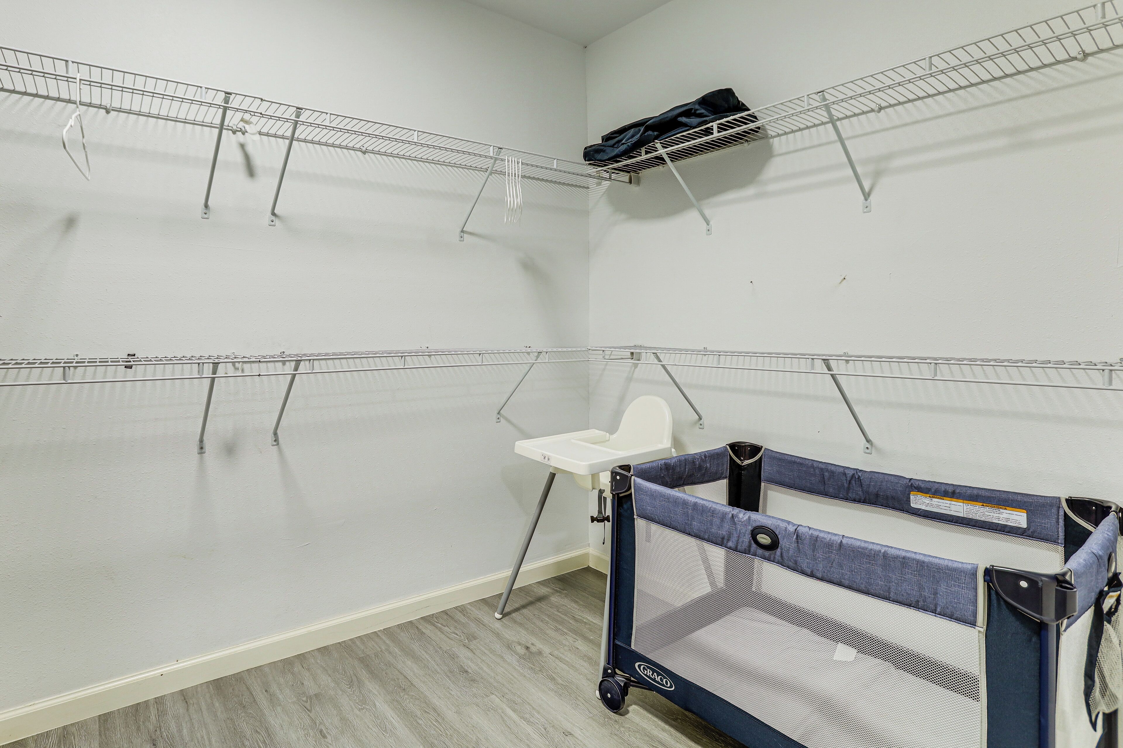 A room with a crib, a white high chair, and metal shelves against the walls.