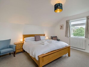 A bedroom with a wooden bed, bedside tables, a chair, a window with curtains, and a wall-mounted lamp. - 5 Bed in Hawkshead (oc-llh55) (Outgate)