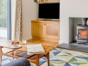 A cozy living room with a wooden table, a map, a glass of water, and a fireplace. - 5 Bed in Hawkshead (oc-llh55) (Outgate)