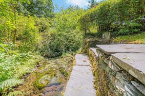 A concrete pathway alongside a small stream in a wooded area. - 4 Bed in Hawkshead (oc-llh44) (Claife)