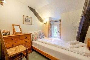 A bedroom with a wooden dresser, a bed, a small table with a mirror, a framed picture on the wall, and a window with curtains. - 4 Bed in Hawkshead (oc-llh44) (Claife)