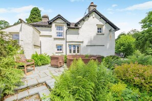 A two-story house with a stone patio and lush greenery. - 4 Bed in Hawkshead (oc-llh44) (Claife)