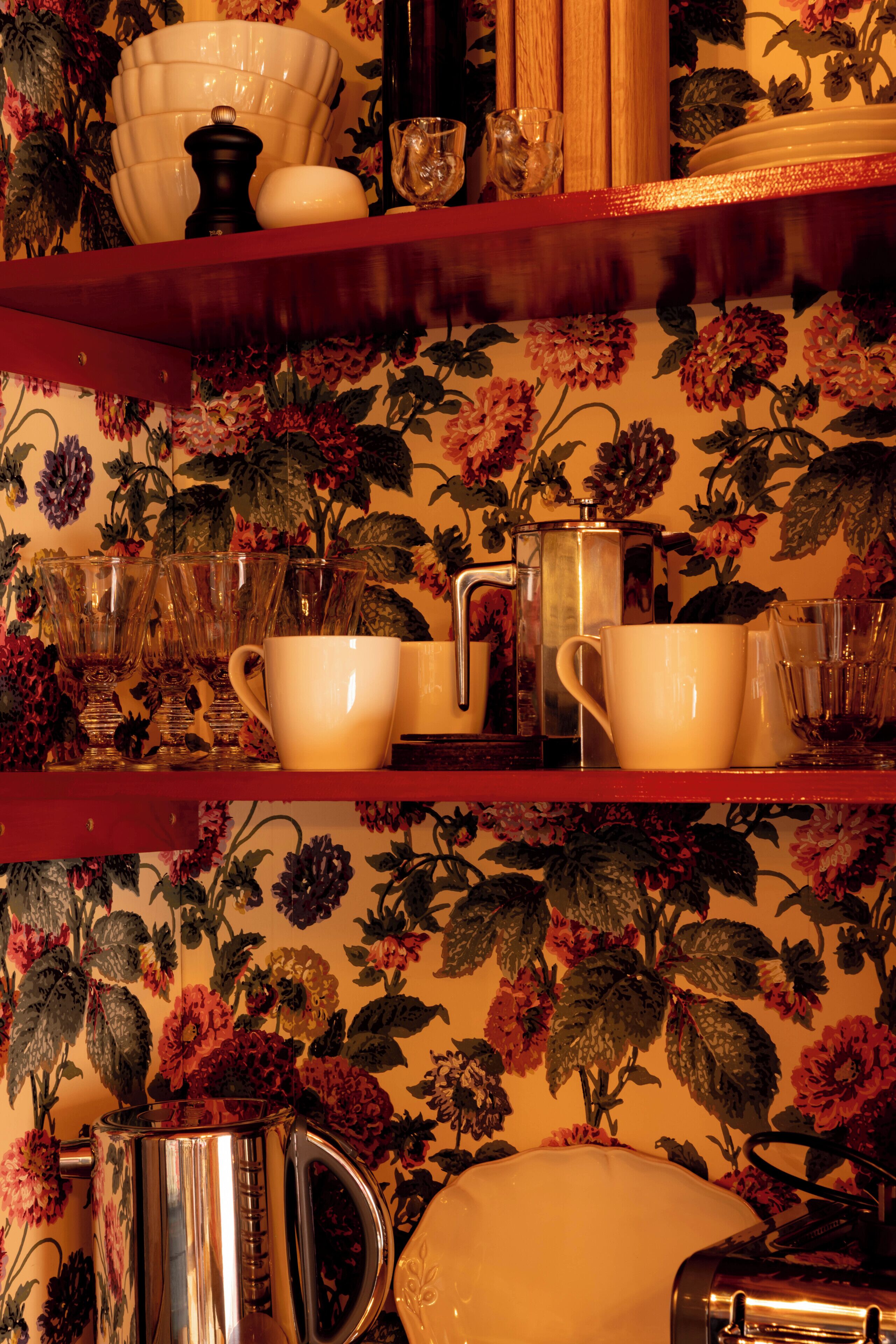 A kitchen area with a floral wallpaper, a coffee maker, and various kitchenware on shelves.