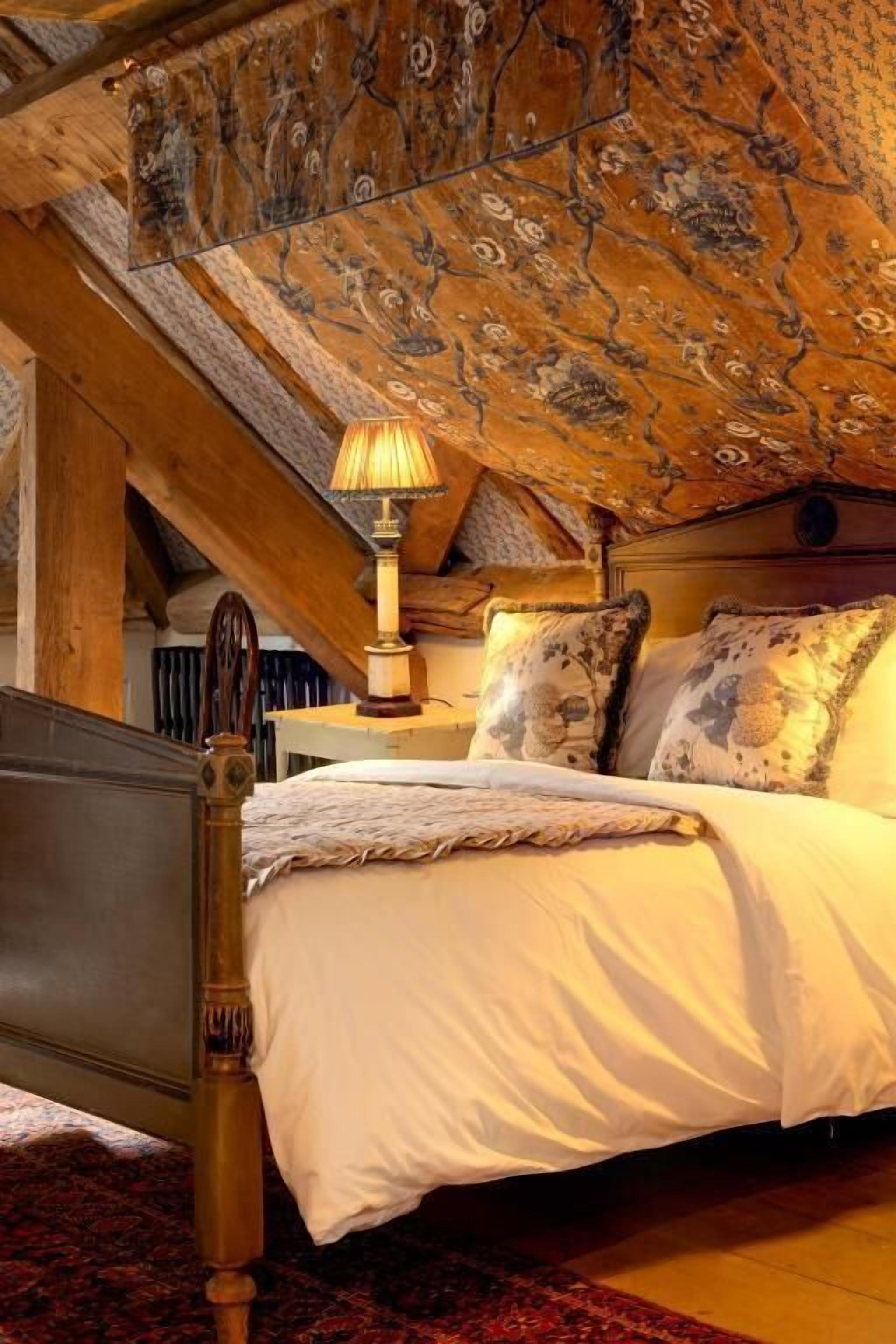 A bedroom with a wooden bed frame, a white bedspread, and a patterned ceiling.