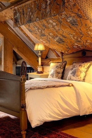 Quarto com estrutura de cama de madeira, colcha branca e teto estampado.