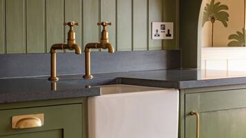 A kitchen with green cabinets, a white sink, and brass faucets.