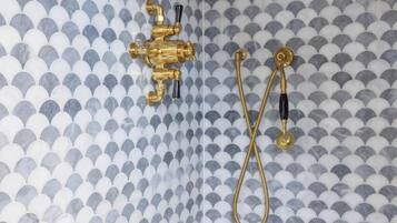 A bathroom with a patterned tile wall, a gold faucet, and a handheld showerhead.