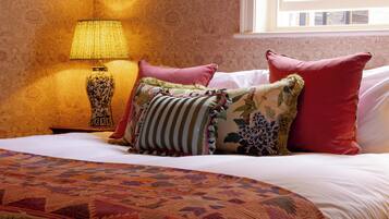 A bed with patterned bedding, a lamp, and pillows against a wallpapered wall.