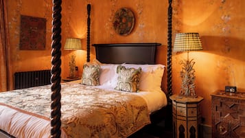Una cama con dosel adornada con ropa de cama ornamentada, dos lámparas fijadas a la pared y un espejo decorativo.