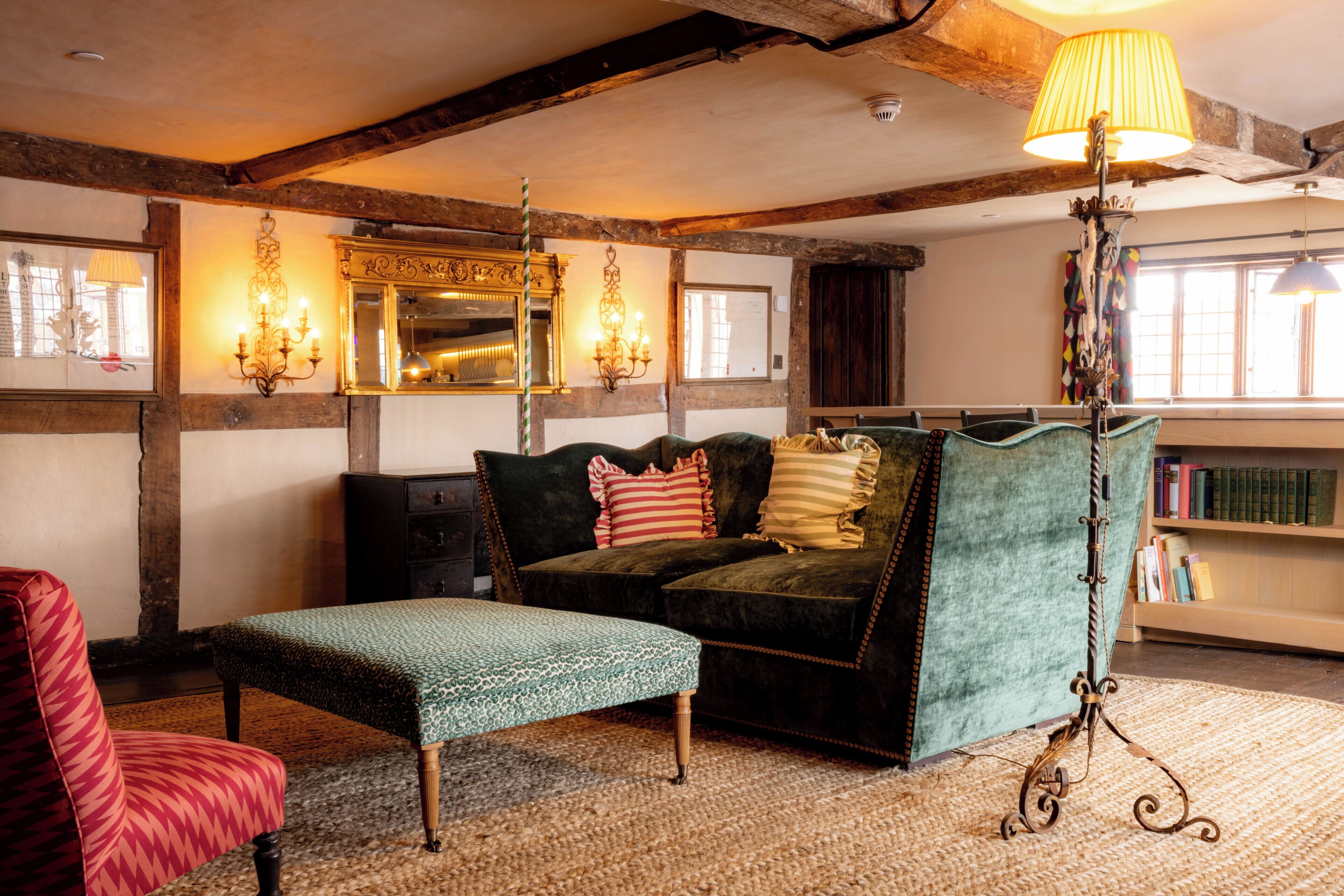 Una habitación acogedora con sofá, un reposapiés estampado, una lámpara de pie y una estantería.