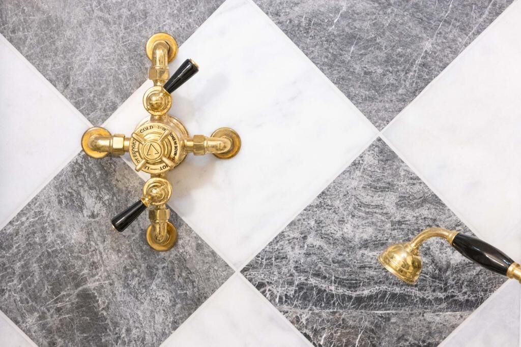 Ein Badezimmer mit goldenem Wasserhahn und einer Handbrause auf einem Marmorboden.