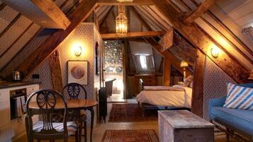 A cozy attic bedroom with a wooden ceiling, a bed, a sofa, and a dining area with chairs.