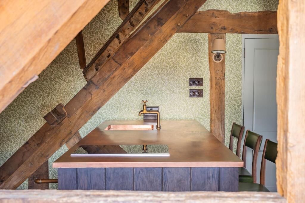 Een rustieke houten eethoek met een inbouwspoelbak, houten balken en uitzicht op de aangrenzende ruimte.