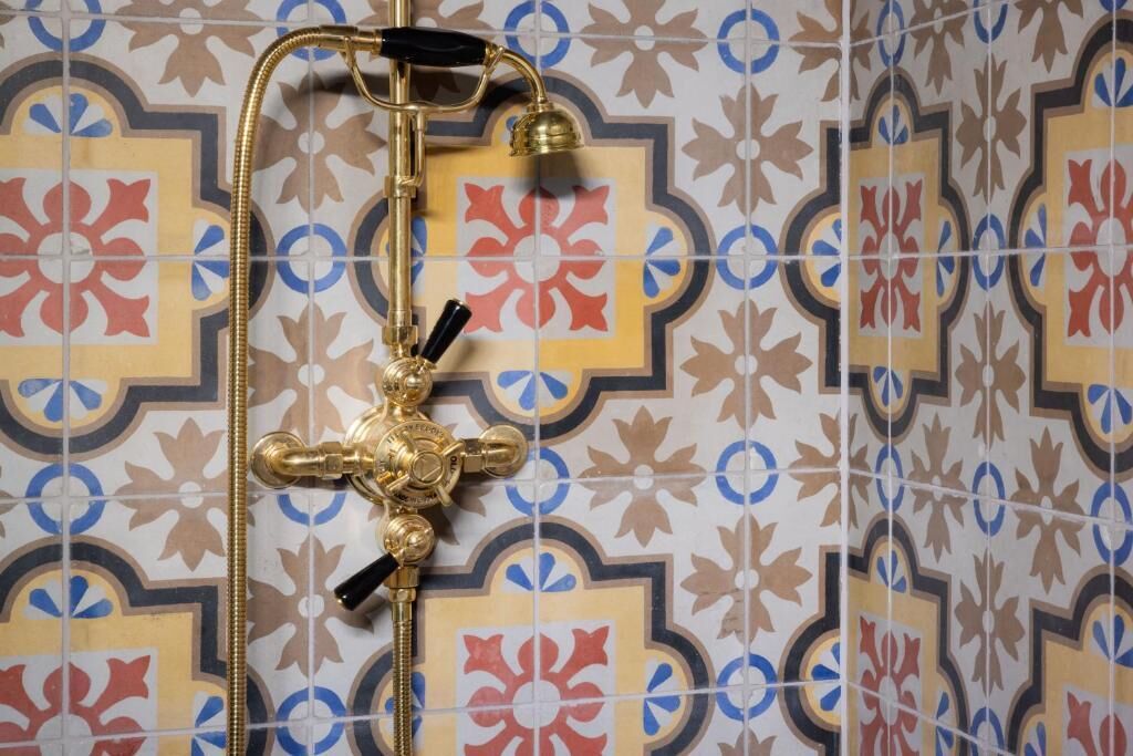 Un baño con un cabezal de ducha decorativo y un pared con azulejos estampados.