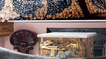 Une baignoire au design rétro, un mur décoratif orné d’un motif en mosaïque et une chaise en bois.