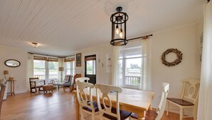 A dining area with a wooden table and chairs, a hanging light fixture, and a view of the outdoors through large windows.