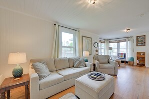 Ein Wohnzimmer mit einer Couch, einem Sessel, einem Hocker und einem Beistelltisch mit einer Lampe.