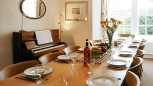 Ett matrum med ett piano, ett bord dukat för sex personer med tallrikar, glas och en vinflaska.