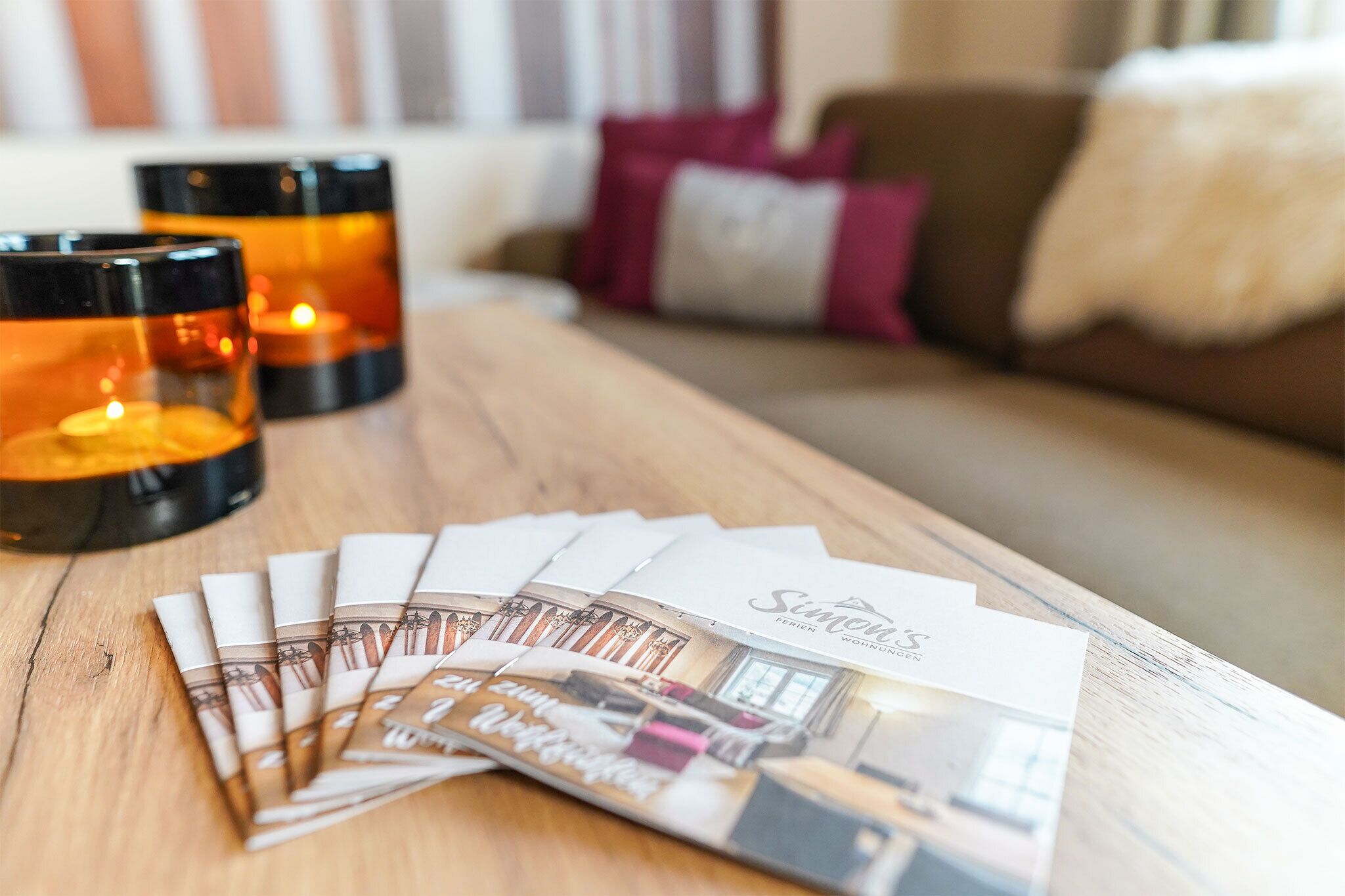 A wooden table with candles, a magazine, and a white card with text.